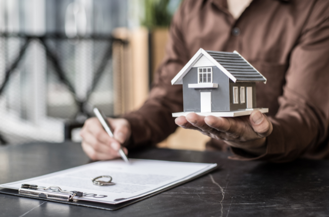 Homeowner signing papers while holding a model house to show how to choose an ADU lender